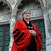 A woman wearing a red and black liturgical vestment, stands outside the majestic Cathedral of St. John the Divine in New York City.