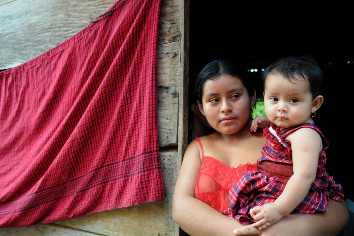 An indigenous Mayan woman holds her daughter outside their home in rural Guatemala while waiting for a community health worker.