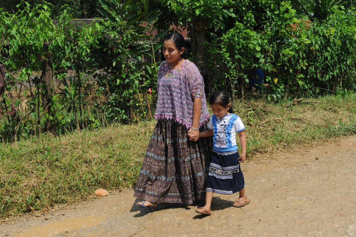 A pregnant indigenous Mayan woman walks home along a rural road, with her young daughter, after a visit to a health center.