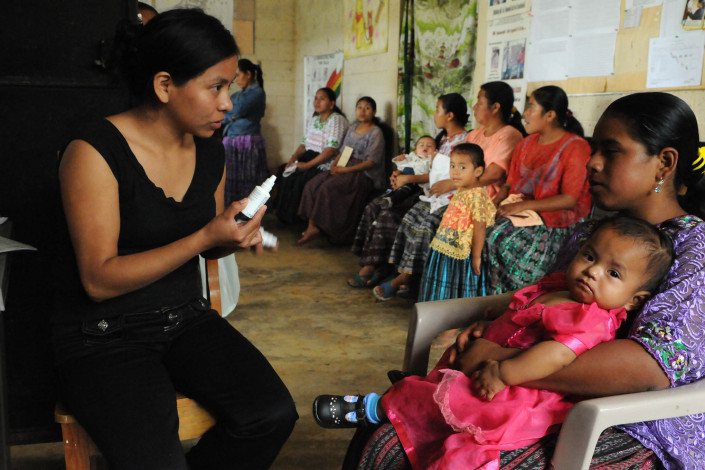 A health worker holding a bottle of medication, advises an indigenous Mayan woman holding her 1-year-old daughter, about the correct use of acetaminophen, in rural Guatemala.