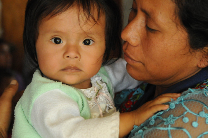 An indigenous Mayan woman holds her wide-eyed infant daughter in a health center in rural Guatemala.