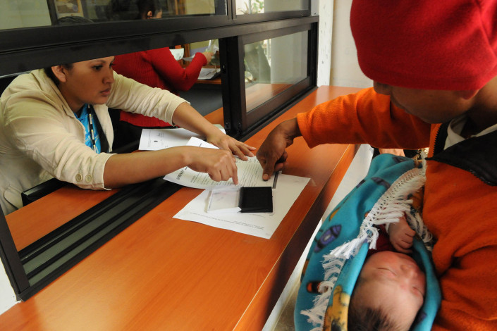 A health worker assists an indigenous Mayan man, holding his newborn son, as he puts his thumbprint on birth registration papers in Guatemala.