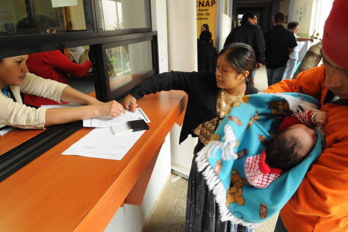 A health worker assists an indigenous Mayan woman, who has just given birth, as she puts her thumbprint on birth registration papers for her newborn son, as her husband stands nearby holding their son.