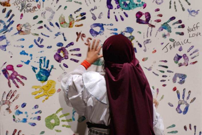 A girl places her painted handprint on a large painting.