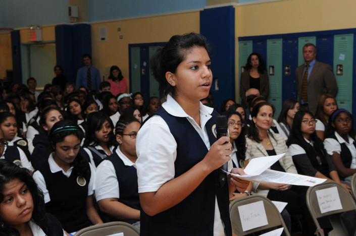 A girl asks a question at a school assembly in an auditorium.