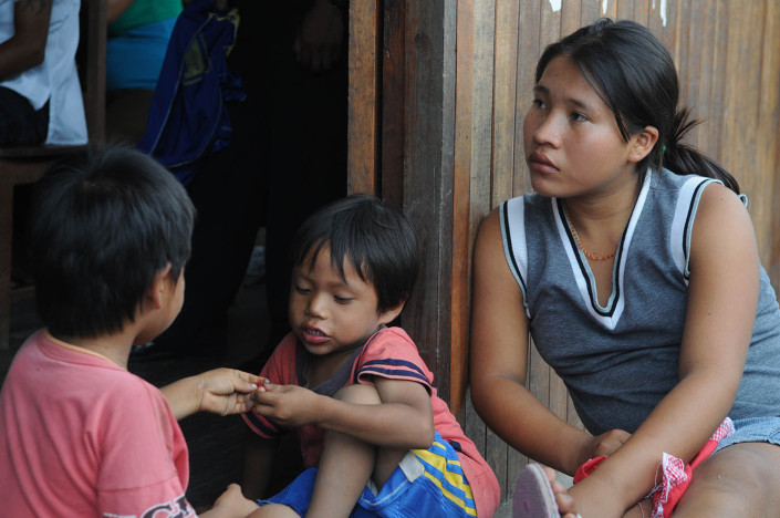 An adolescent girl and 2 young children sit outside a community center in the indigenous Shipibo-Conibo community of Nuevo Saposoa in the Peruvian Amazon.