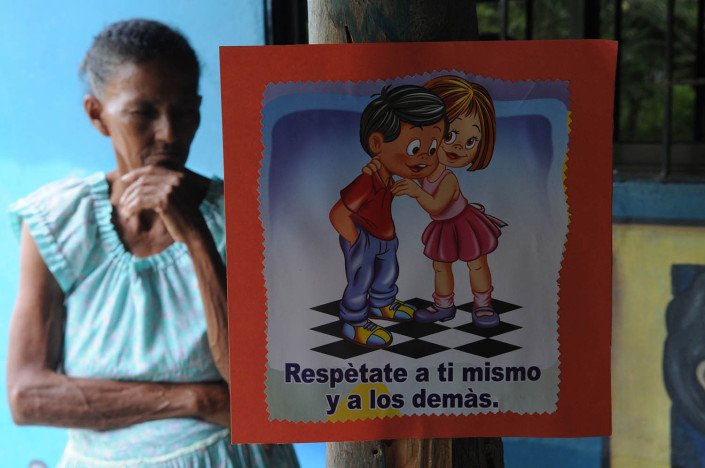 An elderly woman stands behind a sign that says Respect yourself and others, in Spanish, in Colombia .