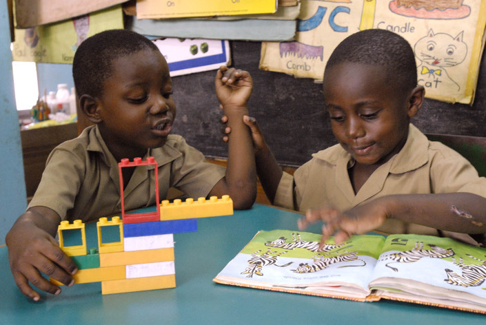 A boy plays with colourful plastic blocks while another boy views a book on counting at a school in the parish of Kingston and St. Andrew, Jamaica.