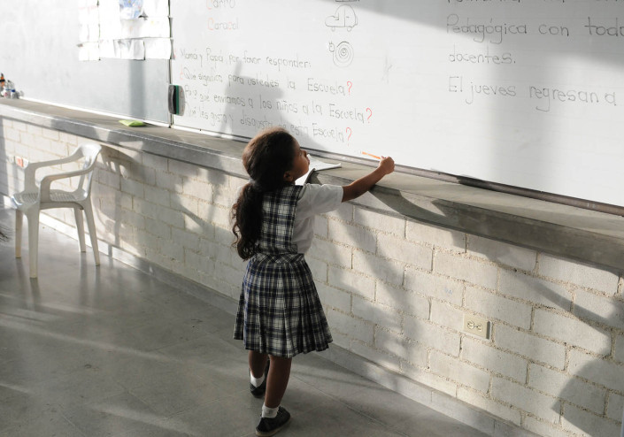 A first grade girl copies homework from the blackboard in Medellín, Colombia.