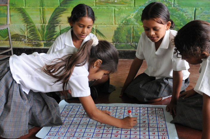 Girls play a word game on the floor, writing words in red marker, on a large sheet of paper in Lorica, Colombia.