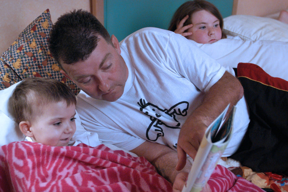 Garry Brooks reads to his daughter Robyn, wrapped in a blanket, in their temporary home at the Ronald McDonald House. She is being treated for neuroblastoma.