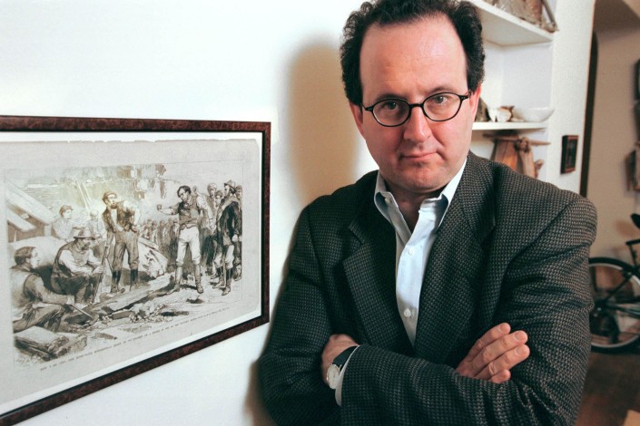 Jonathan Tasini, arms crossed, stands next to a lithograph of a late 19th century lithograph of a workers' protest.