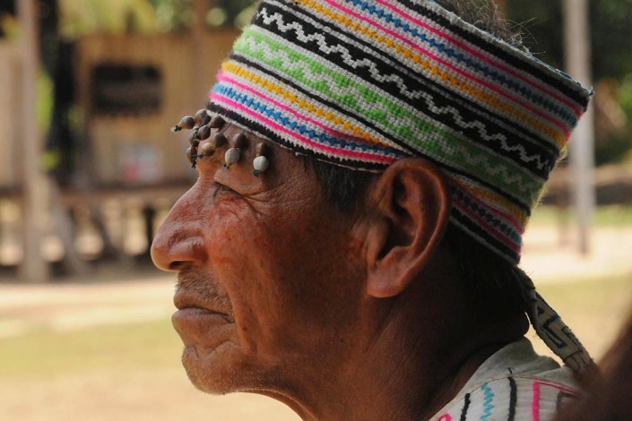 An indigenous Shipibo Conibo community leader, wearing a traditional, colorful and beaded head wrap, painted face and garment, stands outside the community center in Nuevo Saposoa, Peru.