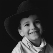 A small boy, wearing a cowboy hat many sizes too large, smiles during a portrait session.