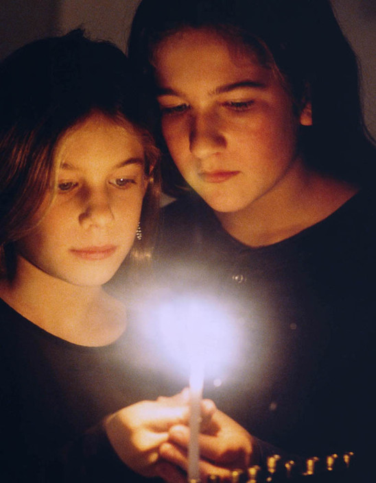 Photograph of sisters Jenny and Danielle lighting a menorah.