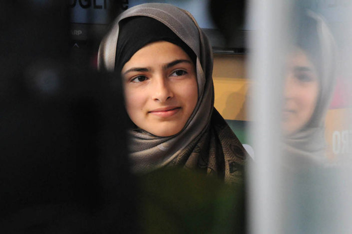 An image of youth activist Minahil Sarfraz, wearing a head scarf, reflected in a window, at UNHQ.