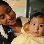 A young mother holds her 8-month-old wide-eyed daughter at a Guatemalan health clinic.