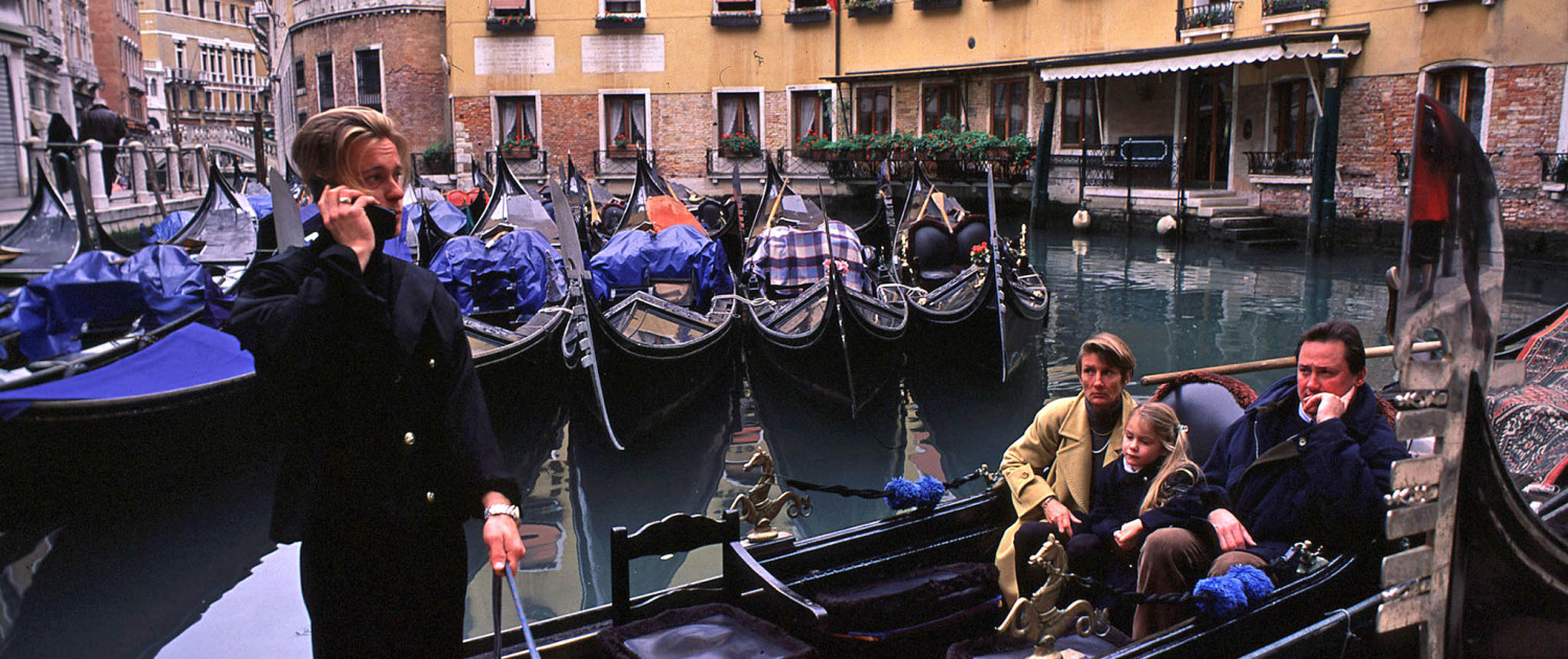 A family waits for a ride in a gondola as the gondolier takes a call on his mobile phone in Venice, Italy.