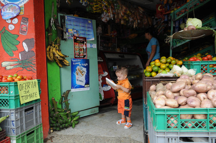 A toddler looks at a package of vegetables in a market in Medellin, Colombia, as his mother shops behind him.