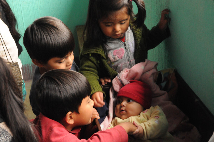Children play with a baby lying in a makeshift crib at a health center in a rural community in Guatemala.