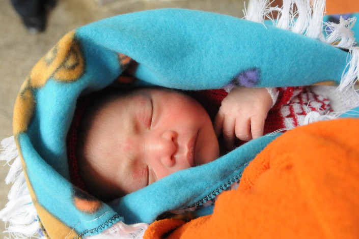 Swaddled in blankets and sleeping, a 1-day-old infant is held by his father, an indigenous Mayan man in Guatemala.
