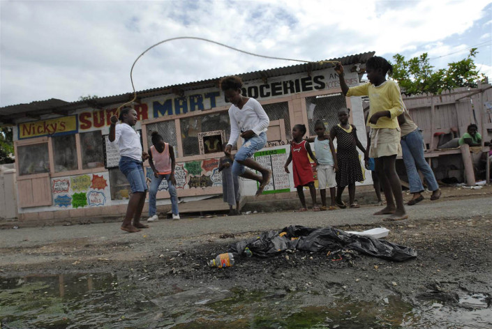 Girls jump rope on a street littered with debris and raw sewage in Trenchtown, in the parish to Kingston and St. Andrew, Jamaica.