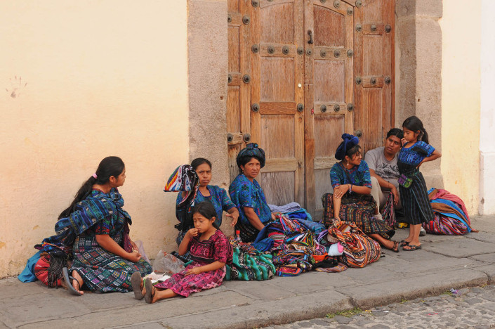 A group of women and children sit on a street in Antigua, Guatemala.
