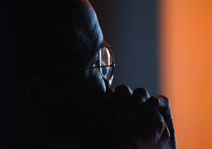 A man backlit by a film screen watches a documentary.