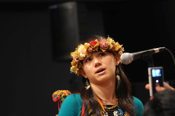 A girl wearing a floral headpiece speaks at an indigenous forum.