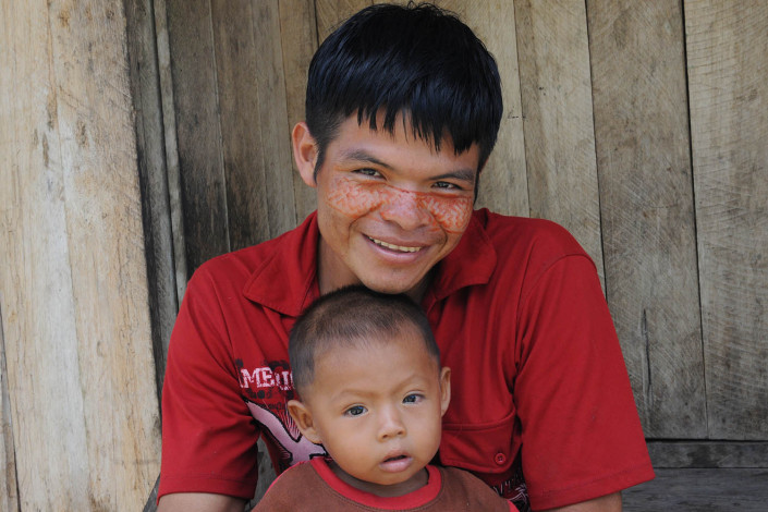 A father wearing paint on his face, and his son, sit outside their home in the indigenous Shipibo-Conibo community of Nuevo Saposoa in the Peruvian Amazon.