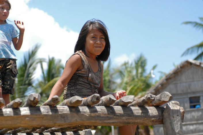 A smiling indigenous Anu girl sits on a wooden dock outside her home above the water, in Laguna de Sinamaica, Venezuela.