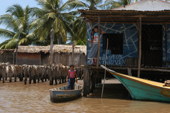 Indigenous Añu siblings stand outside their home, one in a boat, the other above a lagoon, in Laguna de Sinamaica, Venezuela.