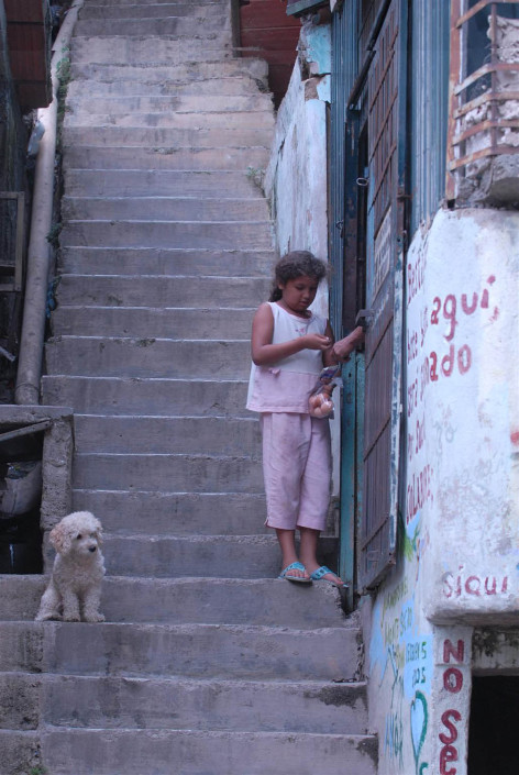 A girl buys eggs from a street vendor, from a shop along a steep concrete staircase, as a small dog watches nearby, in a poor neighborhood of Caracas, Venezuela.