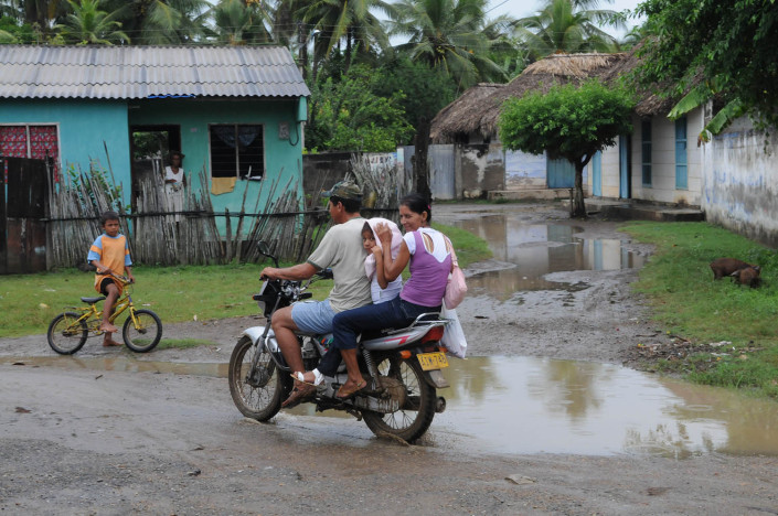A couple with their child on a motorcycle on a flooded rural street in northern Colombia.