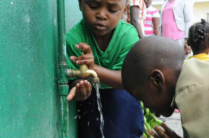 Children wash their hands and faces at an outdoor water point.