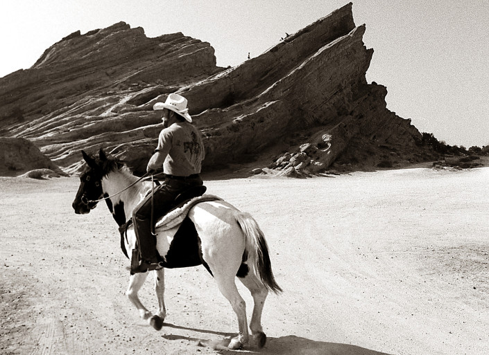 Man with white cowboy hat rides his Palomino horse near Vasquez Rocks in California.