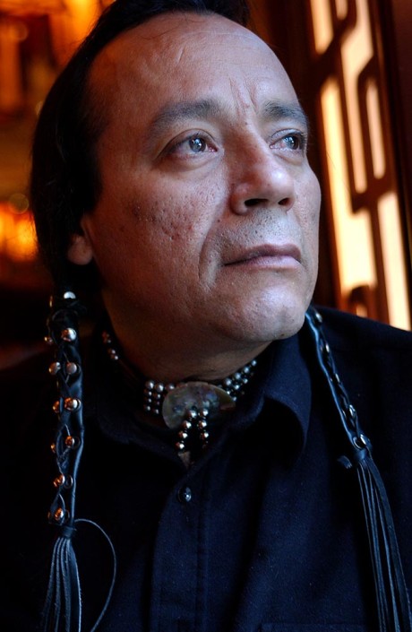 Portrait of native American man with long leather wrapped braids, next to a window.