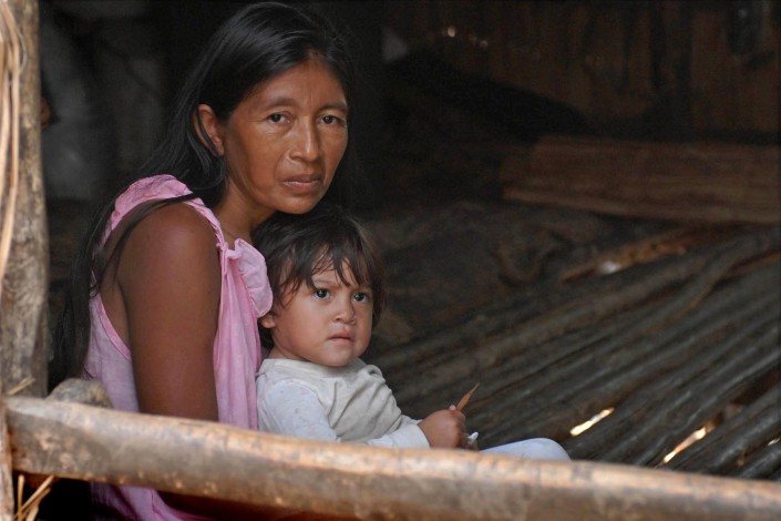 An indigenous Añu woman sits with her 1-year-old daughter in her home made of wooden poles, above a lagoon, in Venezuela.