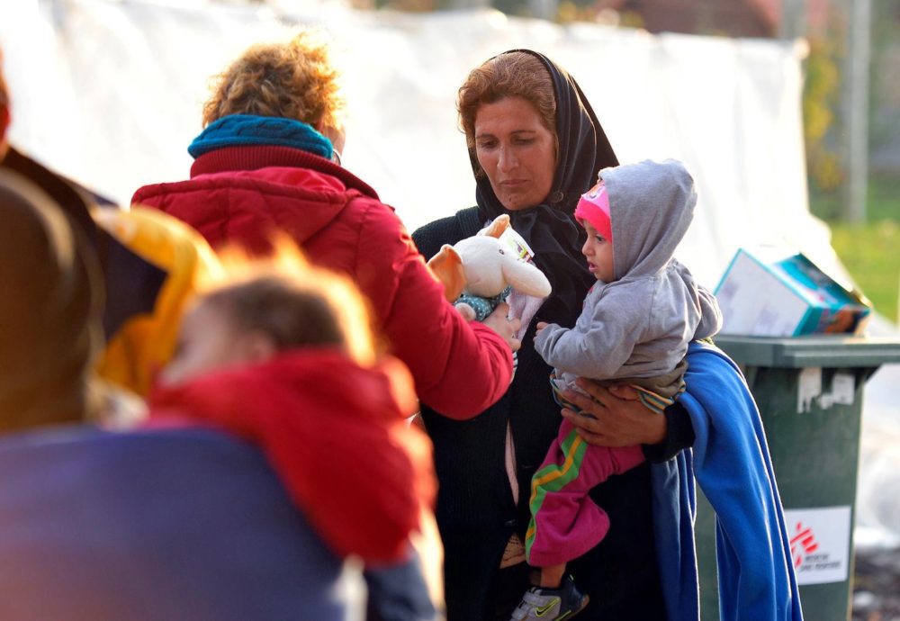medium.com screen capture of refugee woman holding baby, getting toy from an aide worker.