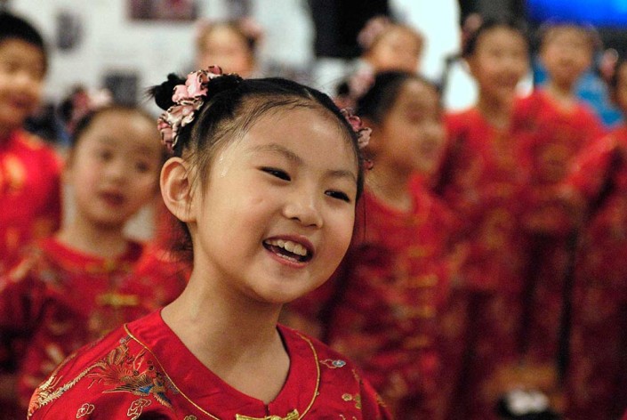 A young Chinese girl dressed in a red satin costume, performs a traditional dance.