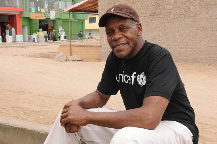 Actor Danny Glover, wearing a UNICEF t-shirt and brown cap, smiles as he sits outside a UNICEF supported childcare center in Lima, Peru.