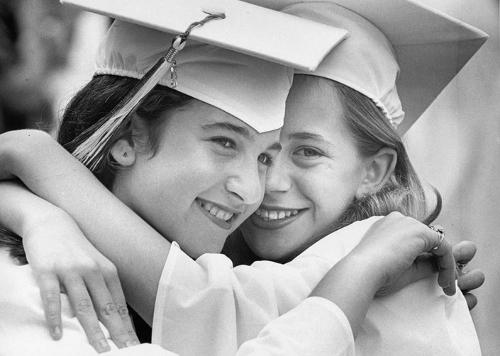 Sisters Danielle and Jennifer Avedon wearing white graduation caps and gowns embrace.