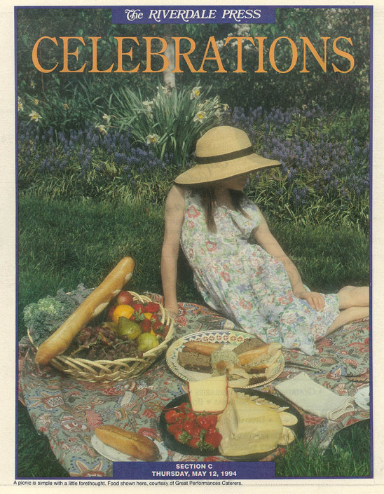 Tear sheet of a newspaper section on Celebrations featuring a girl seated on a colorful blanket with breads, cheeses and fruits.