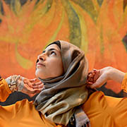 Minahil Sarfraz stands with her arms gently raised, in front of a painted mural echoing the colors of her blouse, at United Nations Headquarters.