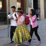 A Bolivian woman wearing a traditional bowler hat and traditional skirt, walk with her son and daughter, in contemporary clothing, along Calle Sacarnaga in La Paz, Bolivia.
